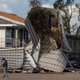 A man walks past a destroyed struture, where aluminum sheets and wooden supports have been twisted by hurricane winds.